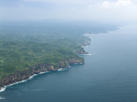 Aerial view of verdant cliffs dropping to the deep blue ocean Gunungkidul Regency Special Region of Yogyakarta Indonesia. Aerial view of verdant cliffs dropping to the deep blue ocean Gunungkidul Regency Special Region of Yogyakarta Indonesia.