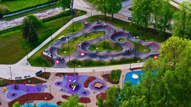 Aerial view of a modern pump track and colorful playground in a park with green trees and paved paths in Latvia. Aerial view of a modern pump track and colorful playground in a park with green trees and paved paths in Latvia.