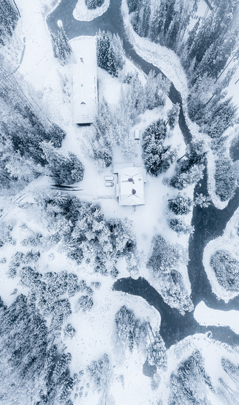 Aerial view of a house nestled in a snow covered forest with a winding river flowing through the landscape in Latvia. Aerial view of a house nestled in a snow covered forest with a winding river flowing through the landscape in Latvia.