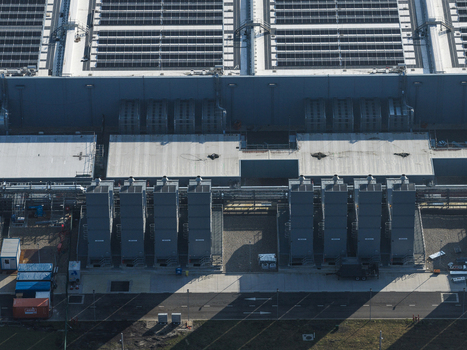 Aerial view of an AI data center with cooling towers and cloud computing hub exterior featuring rooftop infrastructure and industrial cooling systems. Aerial view of an AI data center with cooling towers and cloud computing hub exterior featuring rooftop infrastructure and industrial cooling systems.
