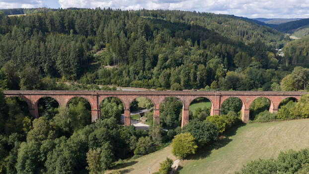 Aerial view of Himbachel Viadukt a historic red sandstone railway bridge spanning a lush green valley with dense forests and meadows in Erbach Hessen Germany.