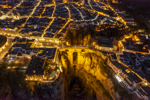 Aerial view of the iconic Puente Nuevo bridge spanning the deep El Tajo gorge in Ronda illuminated at night with warm city lights on the stone architecture Ronda Andalusia Spain. Aerial view of the iconic Puente Nuevo bridge spanning the deep El Tajo gorge in Ronda illuminated at night with warm city lights on the stone architecture Ronda Andalusia Spain.