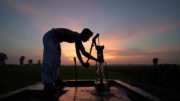 View of a man pumping water at sunset in Bogura Bangladesh. View of a man pumping water at sunset in Bogura Bangladesh.