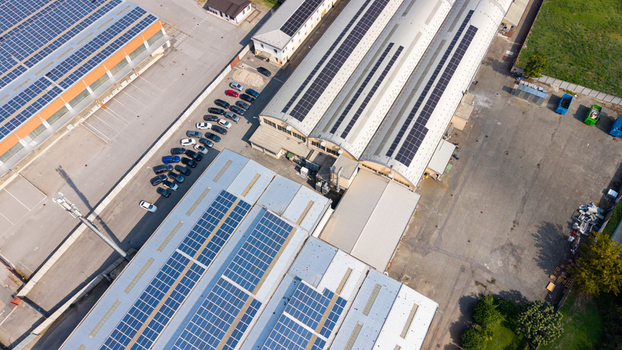 Aerial view of industrial buildings featuring extensive rooftop solar panel arrays a parking lot with parked cars and paved grounds in an industrial zone in Milan Lombardy Italy. Aerial view of industrial buildings featuring extensive rooftop solar panel arrays a parking lot with parked cars and paved grounds in an industrial zone in Milan Lombardy Italy.