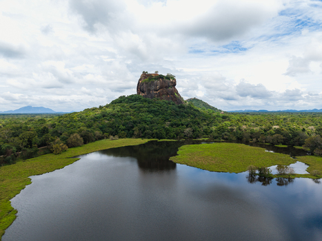 Aerial view of Sigiriya Lion Rock fortress rising above the lush green jungle with a large lake in the foreground under a cloudy sky Sigiriya Central Province Sri Lanka. Aerial view of Sigiriya Lion Rock fortress rising above the lush green jungle with a large lake in the foreground under a cloudy sky Sigiriya Central Province Sri Lanka.