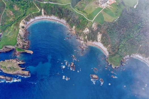 Aerial view of Silence Beach Viewpoint with its crescent shaped bay turquoise waters and dramatic rocky cliffs surrounded by lush green hills Cudillero Asturias Spain.