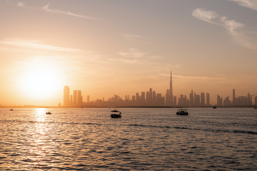 View of shimmering waters reflect the golden hues of a setting sun casting a warm glow over the distant skyline and boats Dubai Dubai United Arab Emirates.