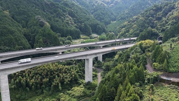 Aerial view of a highway with concrete bridges winding through the lush green mountainous landscape of Shimizu Ward in Shizuoka Shizuoka Japan. Aerial view of a highway with concrete bridges winding through the lush green mountainous landscape of Shimizu Ward in Shizuoka Shizuoka Japan.