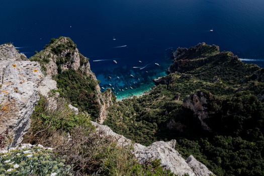 View of the turquoise waters of a bay filled with boats framed by steep green cliffs and the deep blue Mediterranean Sea in Capri Campania Italy. View of the turquoise waters of a bay filled with boats framed by steep green cliffs and the deep blue Mediterranean Sea in Capri Campania Italy.