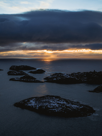 Aerial view of the dark rocks emerging from the still dark sea water under a cloudy sky Henningsv&aelig;r Nordland Norway.