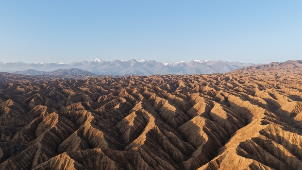 Aerial view of the rugged eroded sandstone formations of the Skazka Canyon landscape with snow capped mountains in the distance in Issyk Kul Region Kyrgyzstan. Aerial view of the rugged eroded sandstone formations of the Skazka Canyon landscape with snow capped mountains in the distance in Issyk Kul Region Kyrgyzstan.