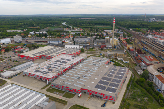 Aerial view of large industrial warehouses with solar panels a tall chimney and railway tracks under a cloudy sky Breclav South Moravian Region Czechia.