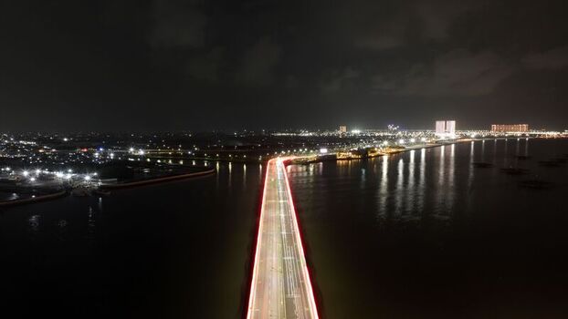 Aerial view of Pantai Indah Kapuk 2 bridge at night with long exposure light trails from traffic and illuminated city skyline in Kecamatan Penjaringan Banten Indonesia. Aerial view of Pantai Indah Kapuk 2 bridge at night with long exposure light trails from traffic and illuminated city skyline in Kecamatan Penjaringan Banten Indonesia.