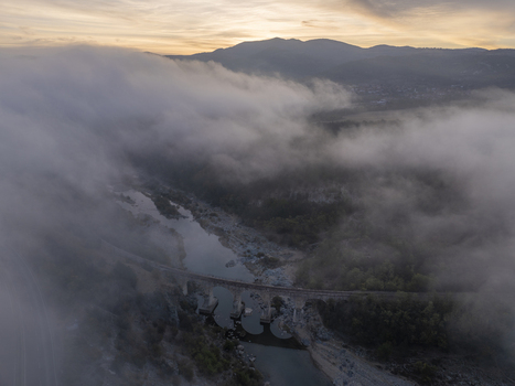 Aerial view of the railway bridge spanning a river amidst dense morning fog with mountains in the background under golden hour light in Balabanovo Kardzhali Province Bulgaria. Aerial view of the railway bridge spanning a river amidst dense morning fog with mountains in the background under golden hour light in Balabanovo Kardzhali Province Bulgaria.