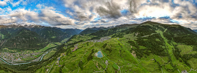 Aerial view of the town of Prutz nestled in the lush green Tyrolean Alps featuring a small mountain lake winding roads and dramatic mountain peaks in Prutz Tyrol Austria. Aerial view of the town of Prutz nestled in the lush green Tyrolean Alps featuring a small mountain lake winding roads and dramatic mountain peaks in Prutz Tyrol Austria.