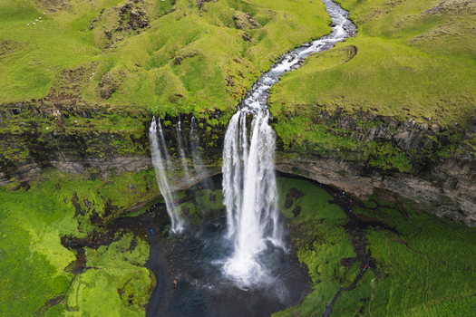 Aerial view of Seljalandsfoss waterfall cascading down a rocky cliff into a pool surrounded by lush green hills and walking paths Rangarthing eystra Iceland. Aerial view of Seljalandsfoss waterfall cascading down a rocky cliff into a pool surrounded by lush green hills and walking paths Rangarthing eystra Iceland.