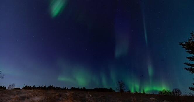 View of vibrant green aurora borealis over a dark landscape Iceland.