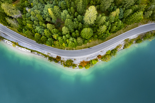 Aerial view of a winding road tracing the edge where a dense forest meets the turquoise waters of Plansee Lake Plansee Tyrol Austria. Aerial view of a winding road tracing the edge where a dense forest meets the turquoise waters of Plansee Lake Plansee Tyrol Austria.