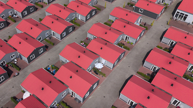Aerial view of prefabricated housing for migrant and seasonal workers with grey houses and red roofs arranged in rows with paved walkways in Swifterbant Flevoland Netherlands. Aerial view of prefabricated housing for migrant and seasonal workers with grey houses and red roofs arranged in rows with paved walkways in Swifterbant Flevoland Netherlands.