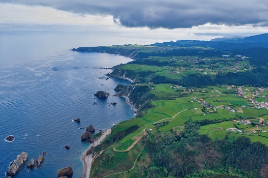 Aerial view of Silence Beach Viewpoint with rugged cliffs green meadows and rocky islets under a cloudy sky in Cudillero Asturias Spain.