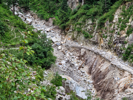 View of the rocky ravine and steep mountain slopes near the village of Malana featuring loose stones boulders and lush green vegetation in Malana Himachal Pradesh India.