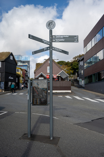 View of a directional street sign and map in Torshavn with traditional wooden buildings featuring grass roofs under a blue sky in the Faroe Islands. View of a directional street sign and map in Torshavn with traditional wooden buildings featuring grass roofs under a blue sky in the Faroe Islands.