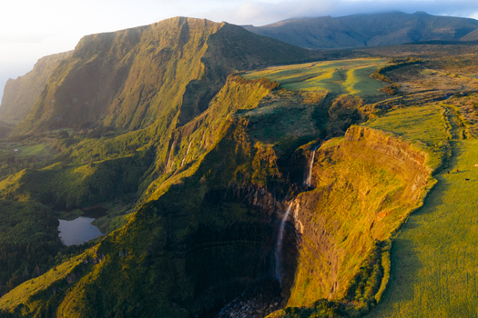 Aerial view of Poco da Ribeira do Ferreiro waterfalls cascading down lush green cliffs during golden hour in Fajazinha Azores Portugal. Aerial view of Poco da Ribeira do Ferreiro waterfalls cascading down lush green cliffs during golden hour in Fajazinha Azores Portugal.