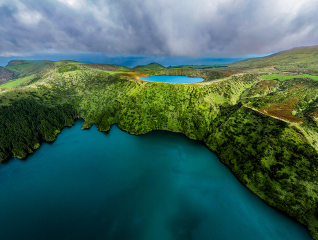 Aerial view of emerald hills embrace the tranquil deep blue waters of Lagoa Comprida under a vast dramatic sky Flores Azores Portugal.