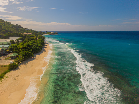 Aerial view of turquoise waters gently kiss the sandy shore framed by verdant trees against a clear blue sky La Retraite Mahe Island Seychelles. Aerial view of turquoise waters gently kiss the sandy shore framed by verdant trees against a clear blue sky La Retraite Mahe Island Seychelles.