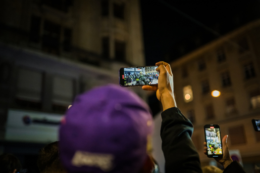 Basel Switzerland 10 March 2025 View of a vibrant street celebration captured on phones a purple hat in the foreground against a backdrop of illuminated buildings. Basel Switzerland 10 March 2025 View of a vibrant street celebration captured on phones a purple hat in the foreground against a backdrop of illuminated buildings.