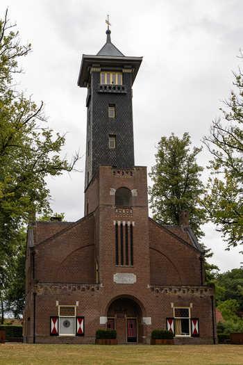 View of De Brandtoren a historic brick fire watch tower with a tall spire and decorative shutters surrounded by trees in Esbeek Noord Brabant Netherlands.