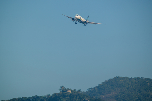 Rio de Janeiro Brazil 06 June 2026 View of a commercial airplane with landing gear down flying over lush green hills against a clear blue sky.