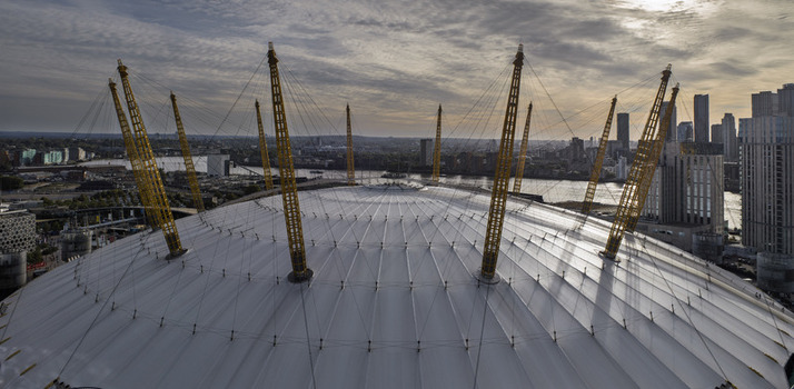 Aerial view of The O2 Arena formerly known as the Millennium Dome featuring its iconic white canopy and yellow support masts under a cloudy sky in London England United Kingdom. Aerial view of The O2 Arena formerly known as the Millennium Dome featuring its iconic white canopy and yellow support masts under a cloudy sky in London England United Kingdom.