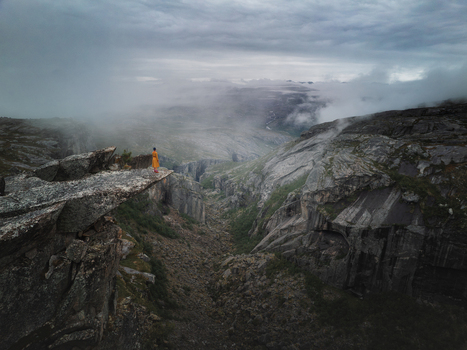 Aerial view of a person in a yellow coat standing on a rocky ledge overlooking the dramatic cliffs and misty depths of Hellmojuvet canyon in Hamaroy Nordland Norway.