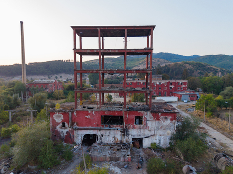 Aerial view of an abandoned red industrial factory with a skeletal multi story structure and a tall chimney surrounded by overgrown vegetation in Velingrad Pazardzhik Bulgaria. Aerial view of an abandoned red industrial factory with a skeletal multi story structure and a tall chimney surrounded by overgrown vegetation in Velingrad Pazardzhik Bulgaria.