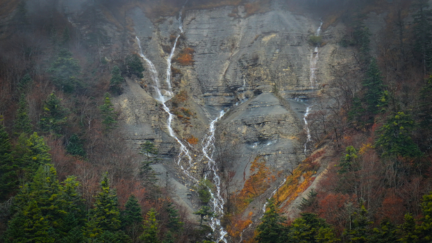 Aerial view of cascading waters gracefully descend the rugged rock face embraced by autumn tinged foliage painting a serene yet dramatic scene Gex Auvergne Rhône Alpes France. Aerial view of cascading waters gracefully descend the rugged rock face embraced by autumn tinged foliage painting a serene yet dramatic scene Gex Auvergne Rhône Alpes France.