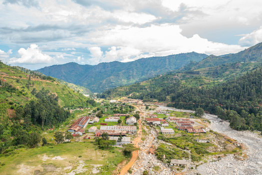 Aerial view of the town of Kilembe nestled in a lush valley with industrial buildings a rocky riverbed and surrounding green mountains in Kilembe Western Region Uganda. Aerial view of the town of Kilembe nestled in a lush valley with industrial buildings a rocky riverbed and surrounding green mountains in Kilembe Western Region Uganda.