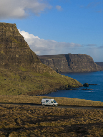 Aerial view of a white camper van parked on a coastal road overlooking dramatic cliffs and the blue sea Isle of Skye United Kingdom. Aerial view of a white camper van parked on a coastal road overlooking dramatic cliffs and the blue sea Isle of Skye United Kingdom.