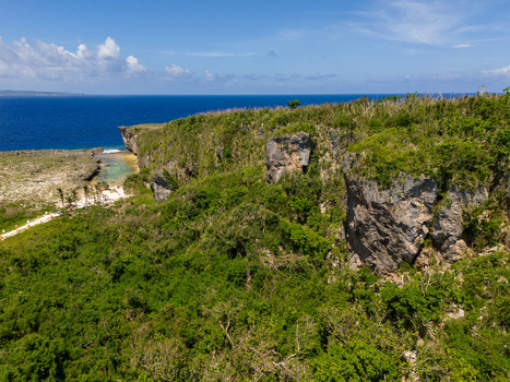 Aerial view of Chigit Beach with rugged limestone cliffs dense tropical vegetation and turquoise waters along the coast in Northern Tinian Tinian Northern Mariana Islands. Aerial view of Chigit Beach with rugged limestone cliffs dense tropical vegetation and turquoise waters along the coast in Northern Tinian Tinian Northern Mariana Islands.