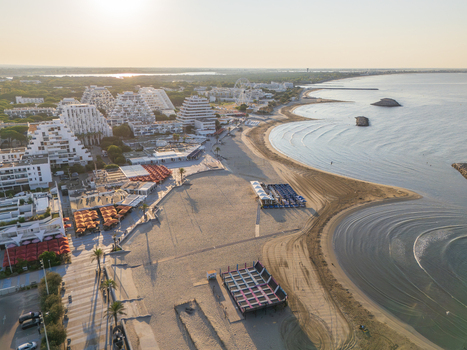 Aerial view of the distinctive pyramid shaped architecture along the sandy Mediterranean coastline with beach umbrellas and calm sea in La Grande Motte Occitanie France.