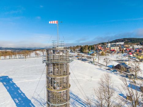 Aerial view of Majak Jary Cimrmana observation tower surrounded by a snow covered landscape and a village under a clear blue sky in Korenov Liberecky kraj Czechia. Aerial view of Majak Jary Cimrmana observation tower surrounded by a snow covered landscape and a village under a clear blue sky in Korenov Liberecky kraj Czechia.