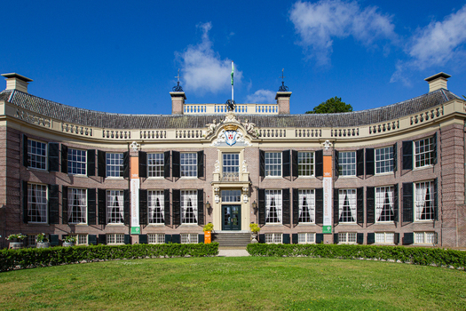 View of the historic curved facade of Castle Groeneveld with its black shutters and white window frames under a blue sky in Baarn Utrecht Netherlands.