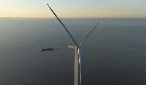 Aerial view of a large wind turbine standing over the calm sea with a cargo ship sailing in the distance during golden hour Netherlands. Aerial view of a large wind turbine standing over the calm sea with a cargo ship sailing in the distance during golden hour Netherlands.
