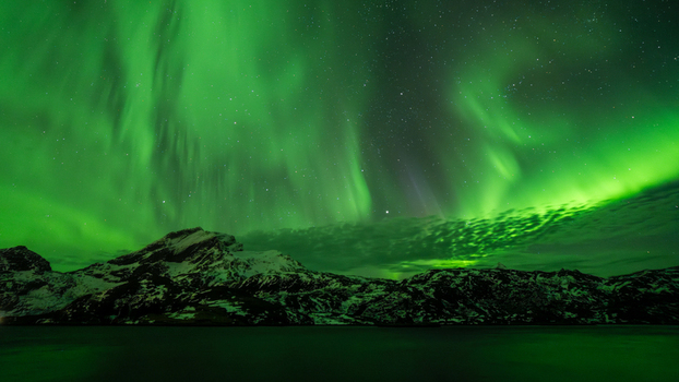 View of vibrant green aurora borealis dancing across the night sky above the rugged snow capped mountains of Leknes Lofoten Norway.
