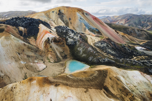 Aerial view of Landmannalaugar rhyolite mountains with a turquoise lake and dark volcanic rocks under a cloudy sky Rangarthing ytra Iceland. Aerial view of Landmannalaugar rhyolite mountains with a turquoise lake and dark volcanic rocks under a cloudy sky Rangarthing ytra Iceland.