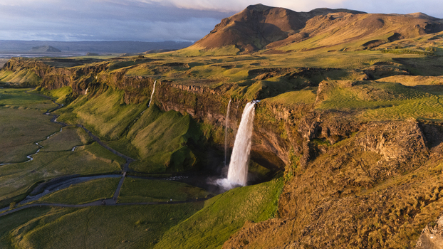 Aerial view of cascading Seljalandsfoss waterfall plunging from verdant cliffs at midnight sun into the Icelandic landscape framed by rugged mountains Seljalandsfoss Iceland. Aerial view of cascading Seljalandsfoss waterfall plunging from verdant cliffs at midnight sun into the Icelandic landscape framed by rugged mountains Seljalandsfoss Iceland.