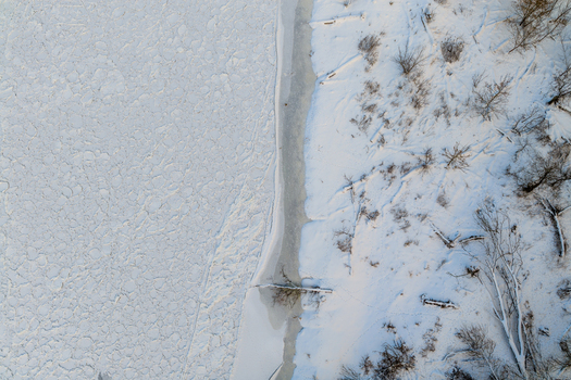 Aerial view of a frozen river with pancake ice floes and a snow covered bank with bare trees Lithuania. Aerial view of a frozen river with pancake ice floes and a snow covered bank with bare trees Lithuania.