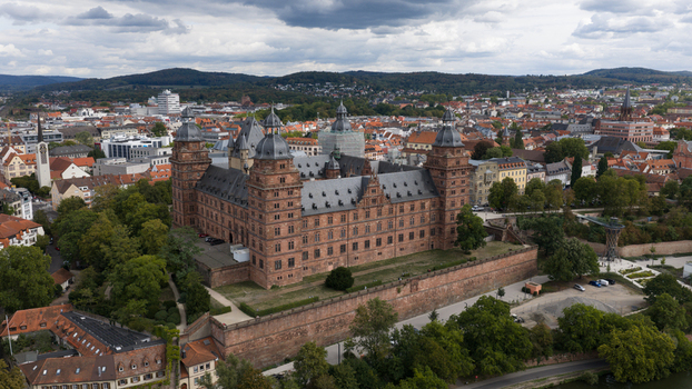 Aerial view of Schloss Johannisburg a historic red sandstone palace surrounded by lush green trees and the cityscape of Aschaffenburg Bayern Germany.