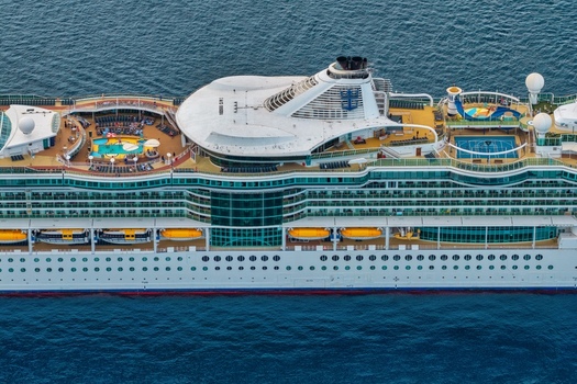 Aerial view of a large cruise ship sailing on the sea featuring multiple decks swimming pools sports courts and lifeboats near Cannes Provence Alpes Cote d Azur France. Aerial view of a large cruise ship sailing on the sea featuring multiple decks swimming pools sports courts and lifeboats near Cannes Provence Alpes Cote d Azur France.