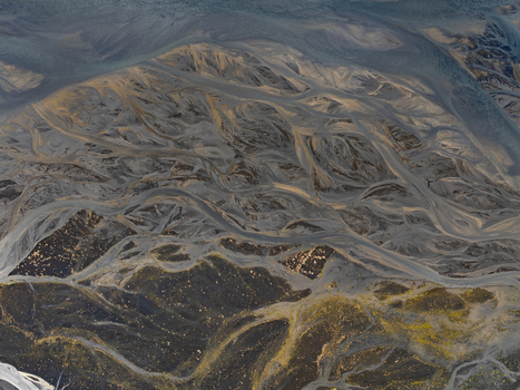 Aerial view of a braided river system with dark volcanic sand and intricate sediment patterns flowing through the landscape of Iceland. Aerial view of a braided river system with dark volcanic sand and intricate sediment patterns flowing through the landscape of Iceland.